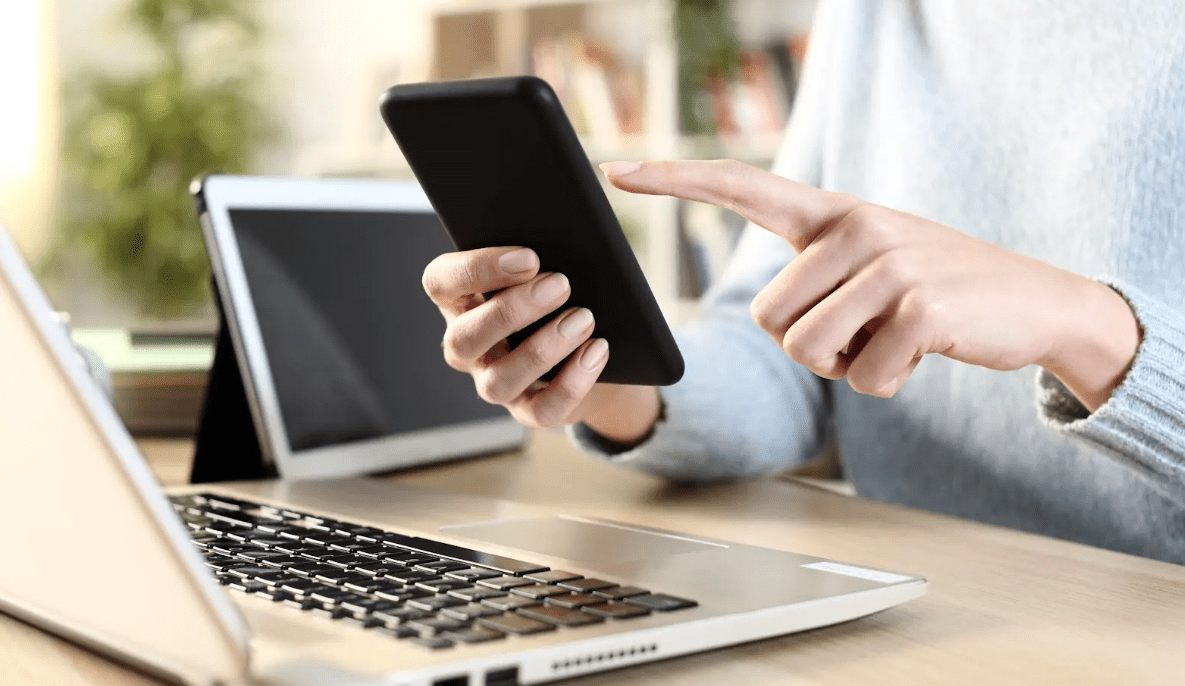 lady at desk holding phone with laptop on desk